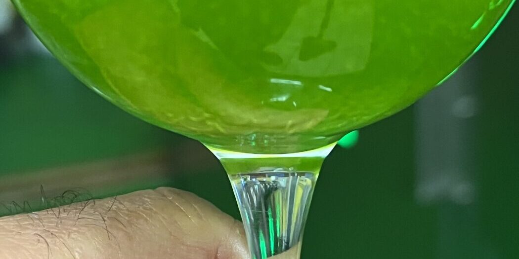 Bicchiere di olio extravergine nuovo 2026 controluce, verde smeraldo e limpido, nel frantoio di Farnese