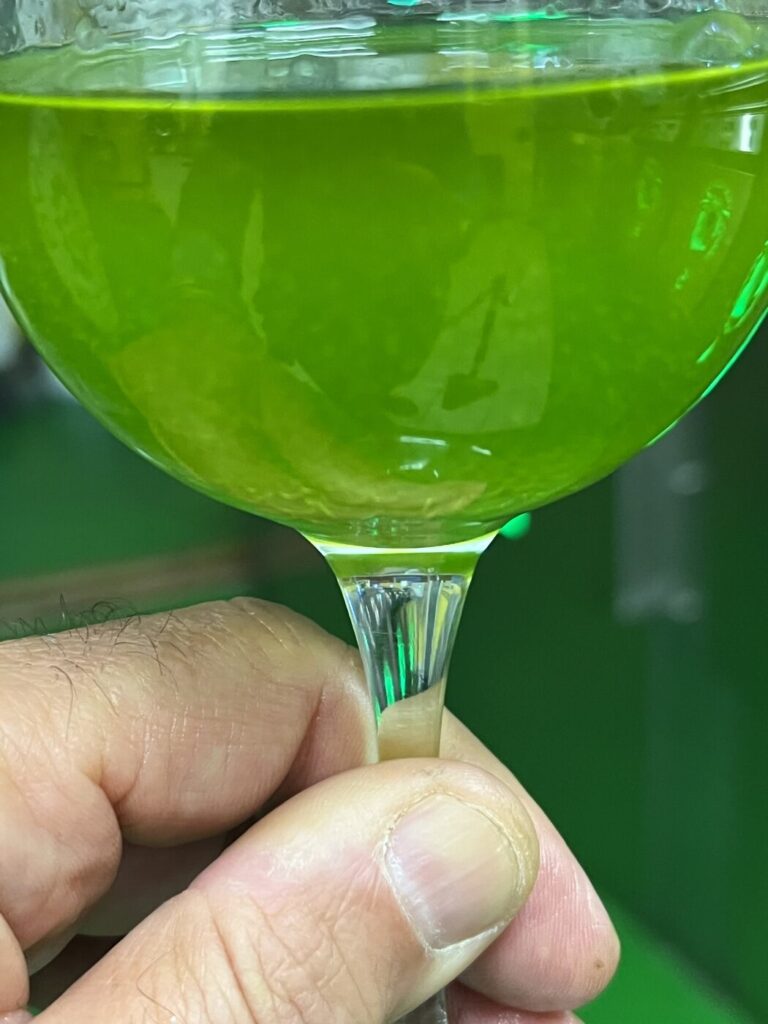 Bicchiere di olio extravergine nuovo 2026 controluce, verde smeraldo e limpido, nel frantoio di Farnese