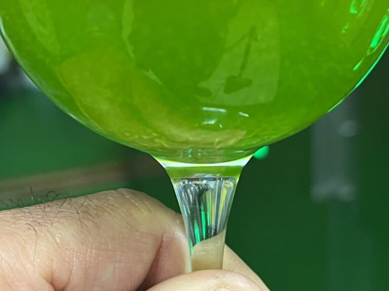 Bicchiere di olio extravergine nuovo 2026 controluce, verde smeraldo e limpido, nel frantoio di Farnese